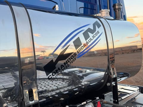Tanque hidráulico cromado com logo Kim Comandos ao pôr do sol
